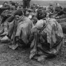 28th March 1945:  Tired and disconsolate German prisoners of war crouch under waterproof capes after their capture on the banks of the Rhine.  (Photo by Fred Ramage/Keystone/Getty Images)
